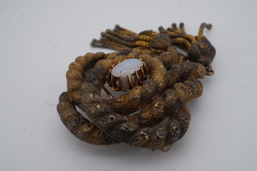 A Victorian opal brooch, mid 19th century, of knotted design in textured gold, set with a cabochon opal, suspending two tassels, length 7cm, gross weight 14 grams